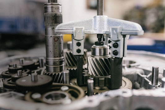 Extractor GEDORE de 2 patas montado sobre un piñón helicoidal dentro de una caja de cambios abierta, rodeado de engranajes y ejes